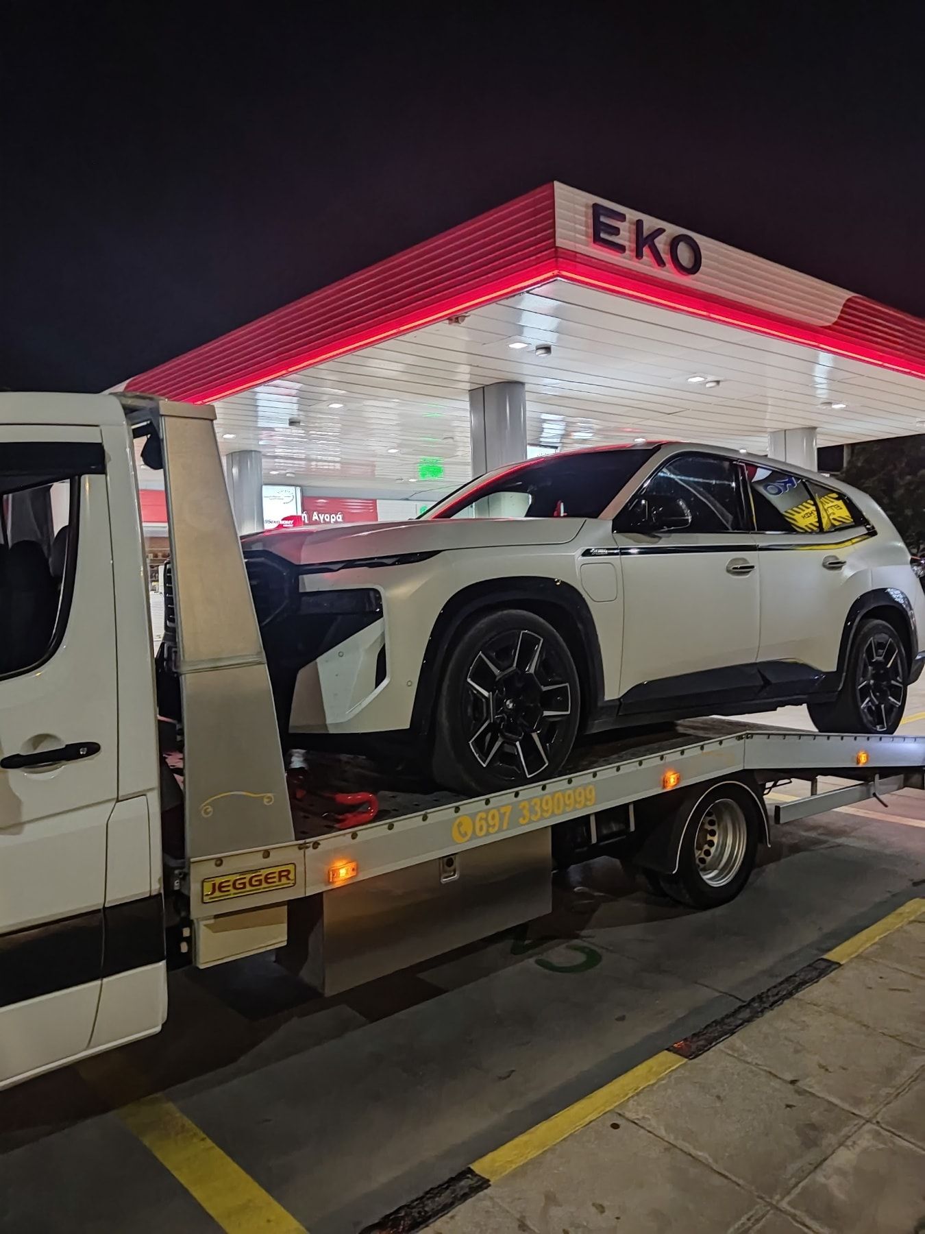 Λευκό BMW XM στην πλατφόρμα της Instant Assistance, τη νύχτα σε πρατήριο καυσίμων